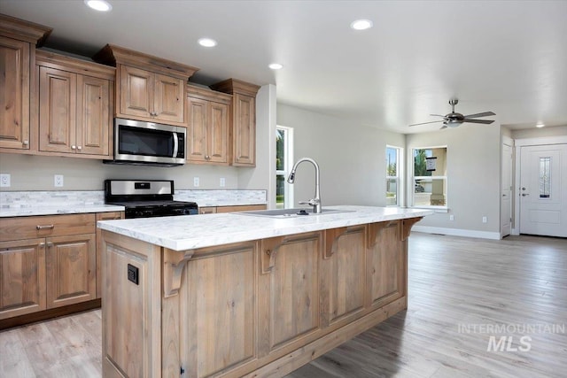 kitchen featuring light hardwood / wood-style floors, sink, ceiling fan, stove, and a kitchen island with sink