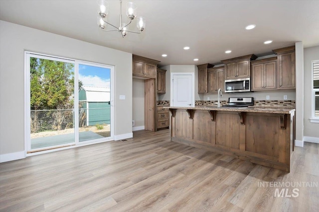 kitchen with a kitchen breakfast bar, range, an inviting chandelier, an island with sink, and light hardwood / wood-style floors