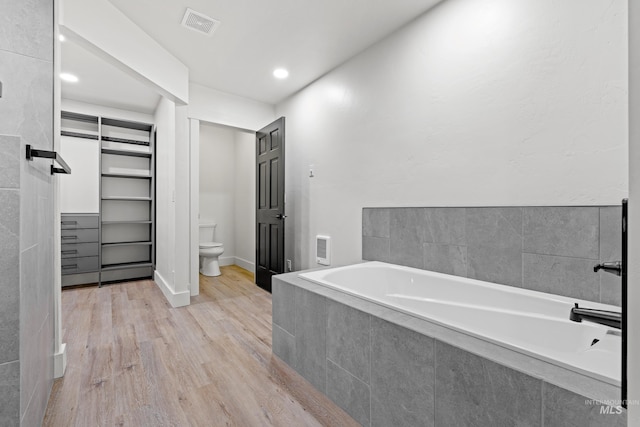 bathroom featuring toilet, wood-type flooring, and tiled bath