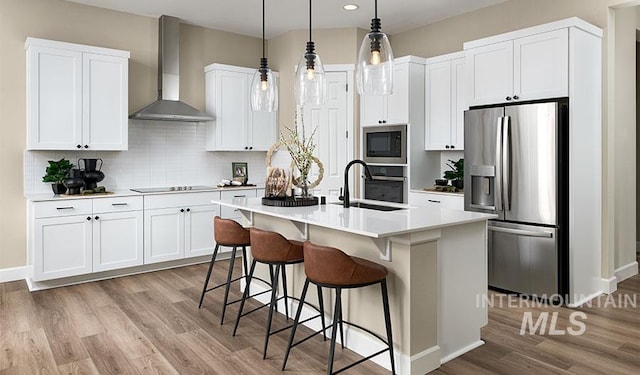 2386 N Ice Fire Ave, Star, ID 83669 - kitchen featuring stainless steel appliances, wall chimney exhaust hood, light wood-type flooring, a kitchen island with sink, and light countertops