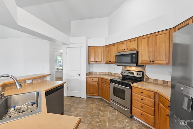kitchen with appliances with stainless steel finishes, a sink, light countertops, and brown cabinets