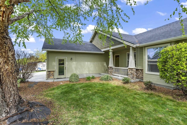 rear view of property featuring a porch, a lawn, stone siding, and a shingled roof