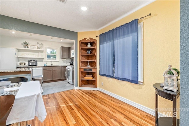 kitchen with open shelves, a sink, white appliances, light wood finished floors, and a textured ceiling