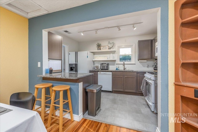 kitchen with white appliances, open shelves, a peninsula, stone counters, and a kitchen breakfast bar