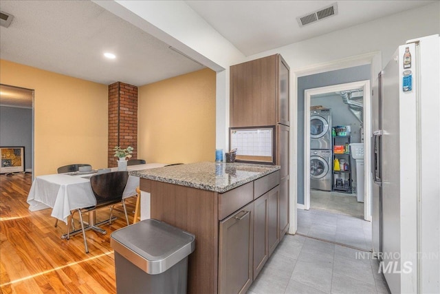 kitchen featuring stacked washer and clothes dryer, light stone counters, freestanding refrigerator, recessed lighting, and baseboards