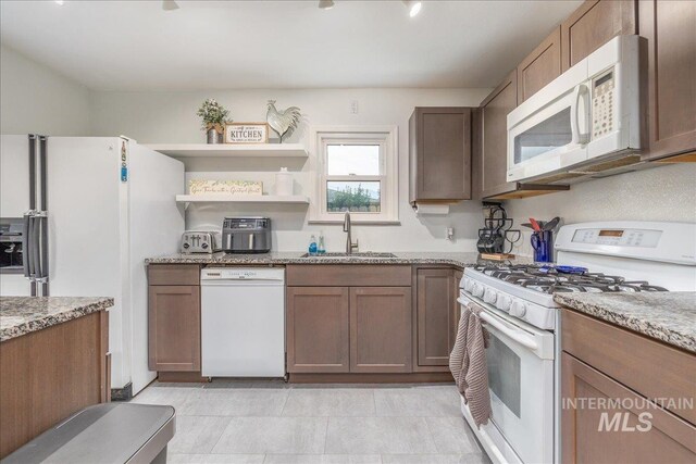kitchen featuring white appliances, a sink, light stone countertops, and open shelves