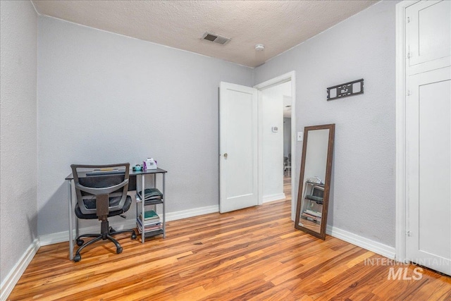 home office featuring light wood-style flooring, baseboards, and a textured ceiling