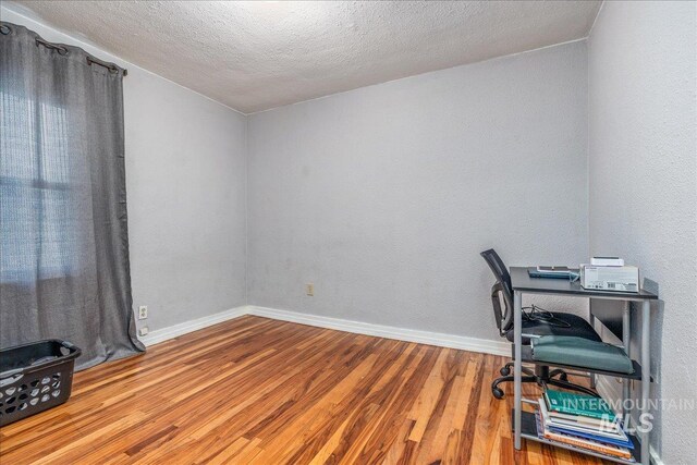 unfurnished office featuring wood finished floors, baseboards, and a textured ceiling