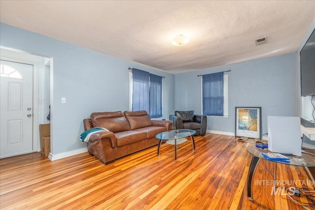 living room featuring light wood-style flooring, baseboards, and a textured ceiling