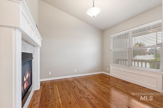 unfurnished living room with light wood-type flooring, a glass covered fireplace, visible vents, vaulted ceiling, and baseboards