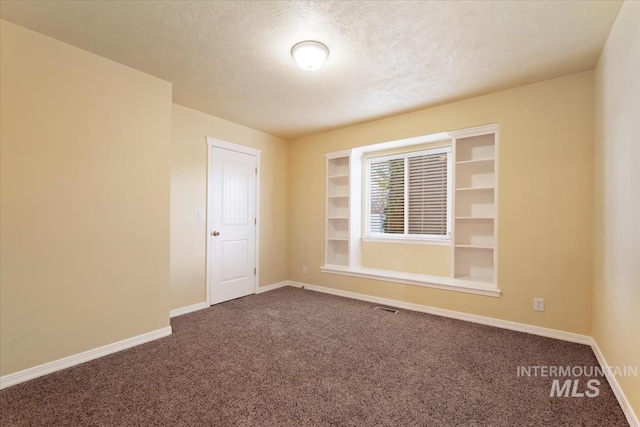 unfurnished room with visible vents, baseboards, dark colored carpet, and a textured ceiling