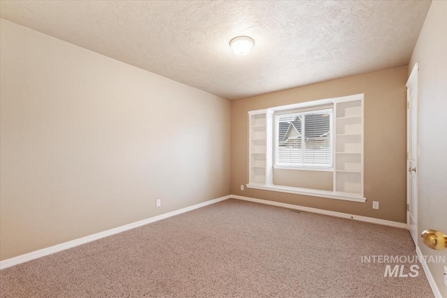 carpeted spare room featuring a textured ceiling and baseboards