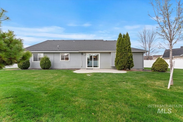 rear view of house with a patio area, a yard, fence, and a shingled roof