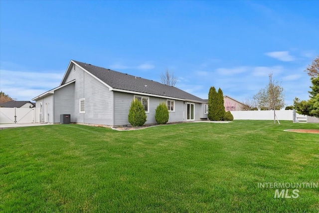 rear view of property featuring central AC unit, fence, a gate, and a lawn