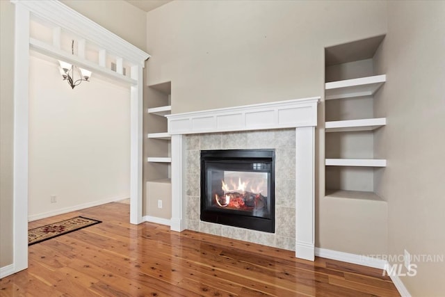 unfurnished living room featuring built in features, baseboards, a tile fireplace, and wood finished floors