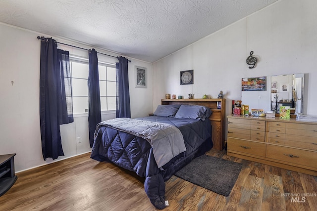 bedroom featuring vaulted ceiling, wood finished floors, and a textured ceiling