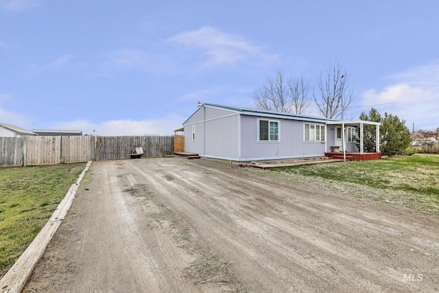 manufactured / mobile home with covered porch, dirt driveway, a front lawn, and fence