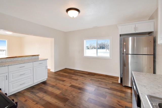 kitchen with dark wood-type flooring, freestanding refrigerator, white cabinets, baseboards, and light stone countertops