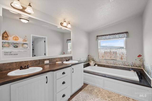 bathroom with a bath, lofted ceiling, and dual bowl vanity