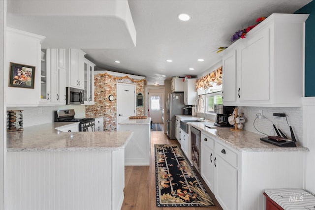 kitchen featuring tasteful backsplash, stainless steel appliances, kitchen peninsula, white cabinetry, and wood-type flooring