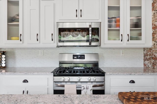 kitchen with white cabinetry, light stone counters, backsplash, and stainless steel appliances