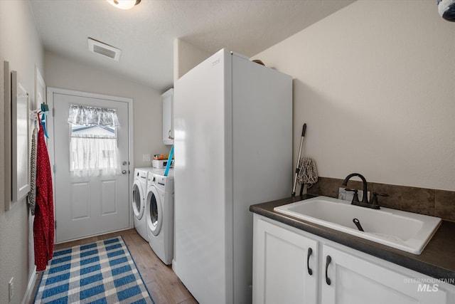 laundry room with washer and clothes dryer, sink, cabinets, light hardwood / wood-style floors, and a textured ceiling