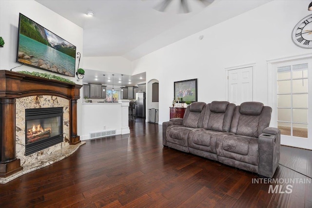 living room featuring arched walkways, high vaulted ceiling, a high end fireplace, visible vents, and dark wood-style floors