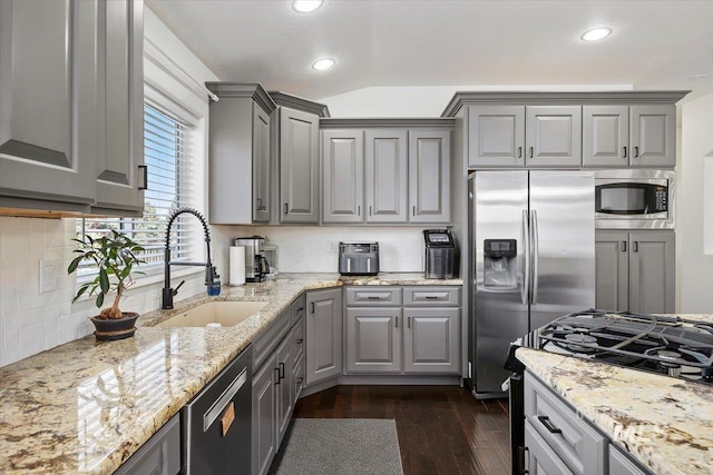 kitchen featuring appliances with stainless steel finishes, a sink, gray cabinetry, and light stone countertops