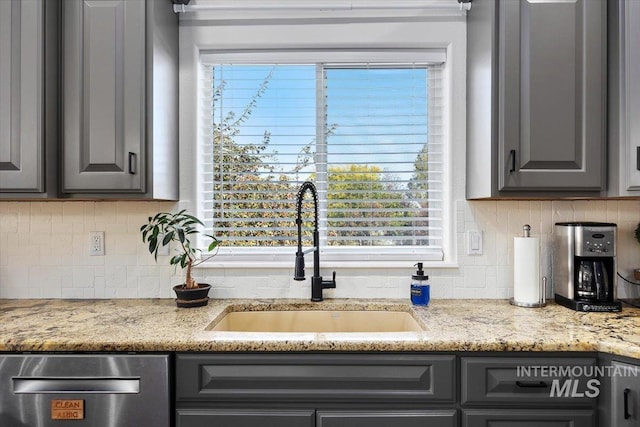 kitchen with decorative backsplash, light stone counters, gray cabinets, and a sink