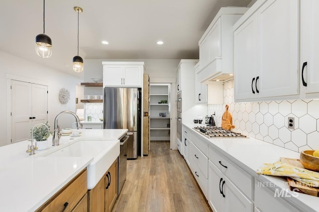 kitchen featuring white cabinetry, stainless steel appliances, tasteful backsplash, pendant lighting, and light hardwood / wood-style floors