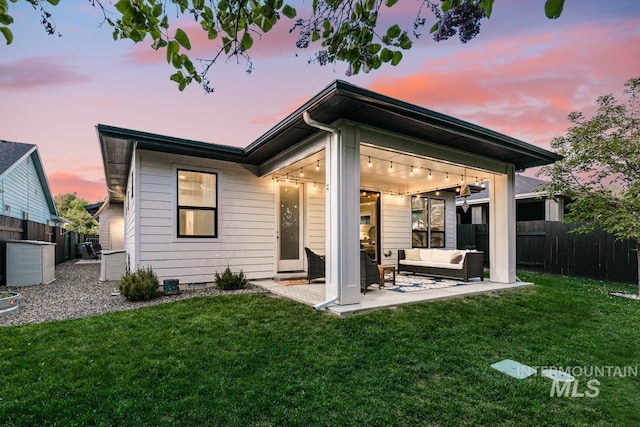 back house at dusk with outdoor lounge area, a yard, and a patio