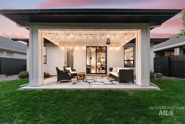 back house at dusk with outdoor lounge area, a yard, and a patio area