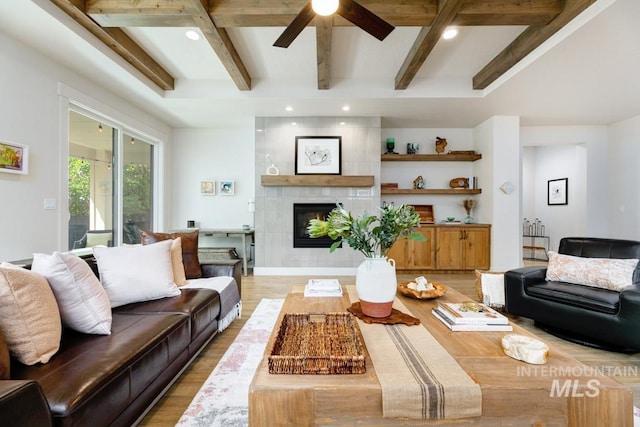 living room with beamed ceiling, hardwood / wood-style floors, a tile fireplace, and ceiling fan