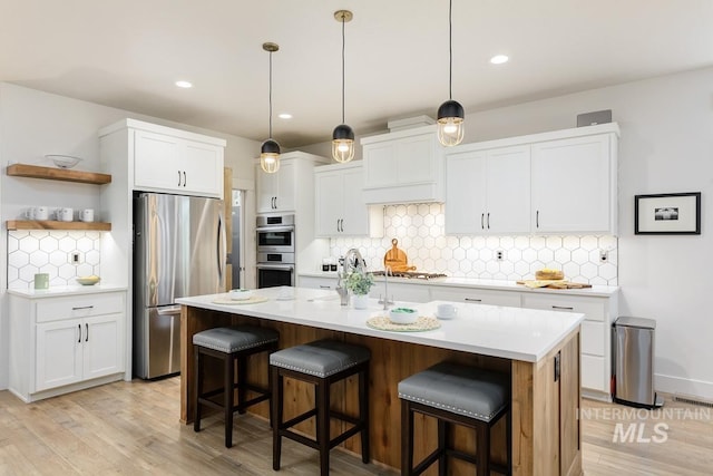 kitchen with a center island with sink, hanging light fixtures, appliances with stainless steel finishes, a kitchen bar, and white cabinetry