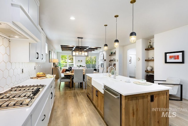 kitchen with white cabinets, decorative backsplash, an island with sink, and appliances with stainless steel finishes