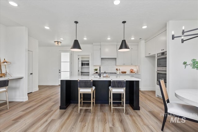 kitchen with white cabinets, pendant lighting, light hardwood / wood-style flooring, and a kitchen island with sink