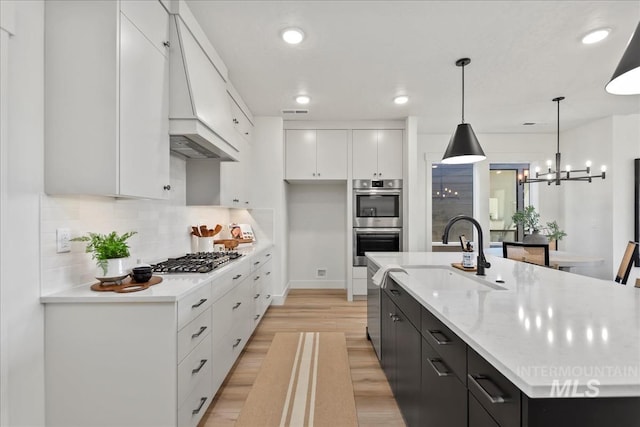 kitchen featuring sink, hanging light fixtures, an island with sink, appliances with stainless steel finishes, and white cabinetry