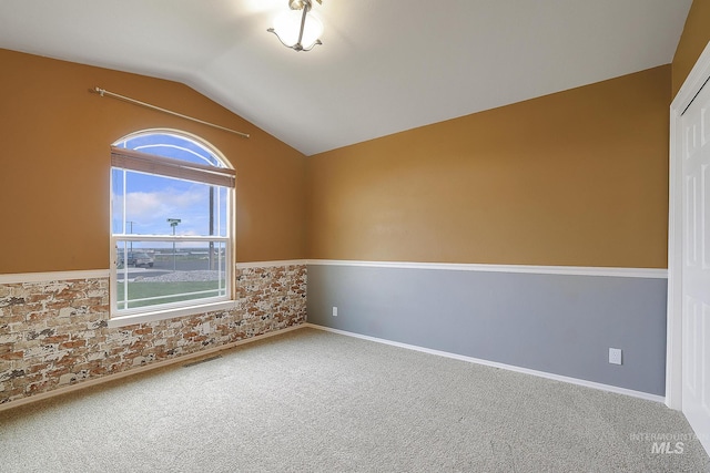 empty room with lofted ceiling, carpet, baseboards, and brick wall