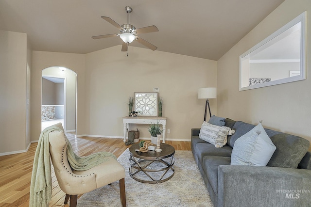 living room with arched walkways, light wood finished floors, ceiling fan, vaulted ceiling, and baseboards