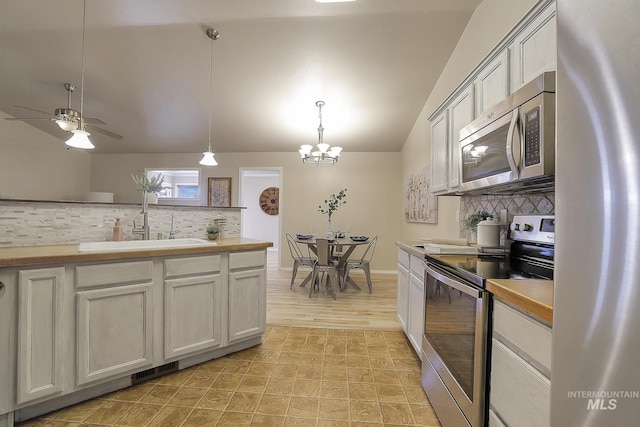 kitchen with appliances with stainless steel finishes, a sink, tasteful backsplash, vaulted ceiling, and hanging light fixtures