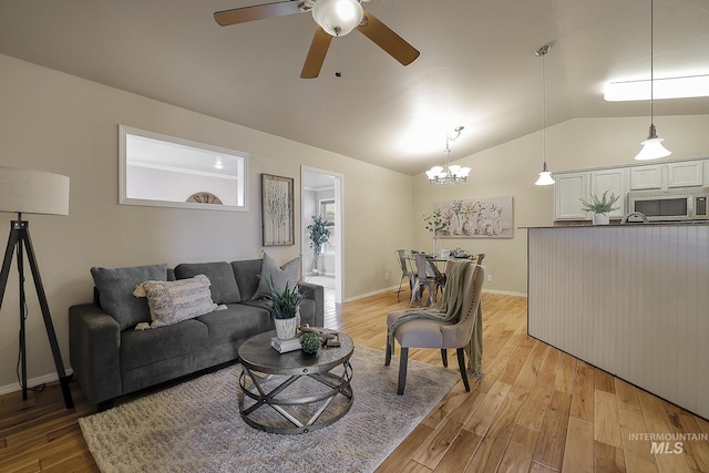 living room featuring vaulted ceiling, ceiling fan, a chandelier, light wood-type flooring, and baseboards