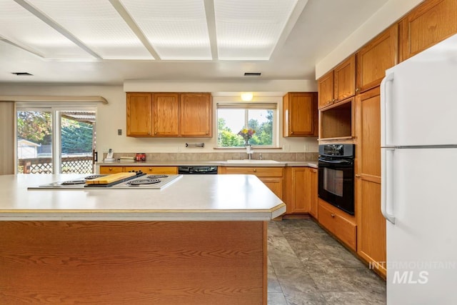 kitchen with black appliances, a sink, light countertops, and brown cabinetry