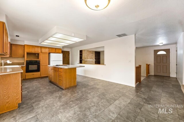 kitchen featuring black oven, freestanding refrigerator, a kitchen island, light countertops, and baseboards