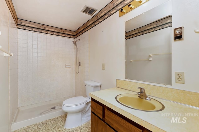 bathroom featuring toilet, tiled shower, vanity, and tile patterned flooring