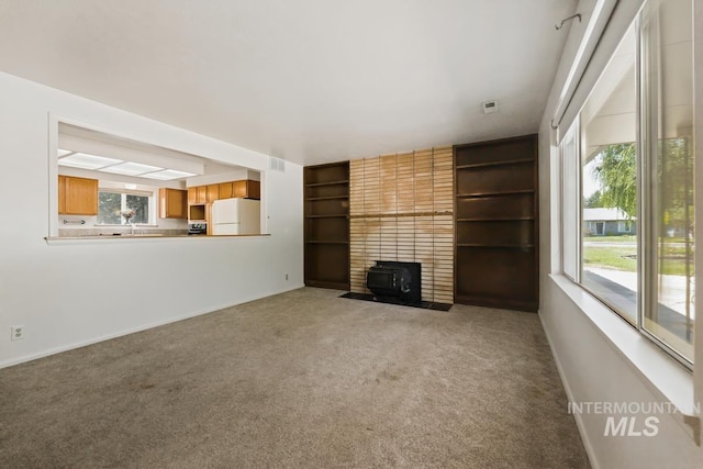 unfurnished living room featuring plenty of natural light, carpet flooring, a wood stove, and built in features