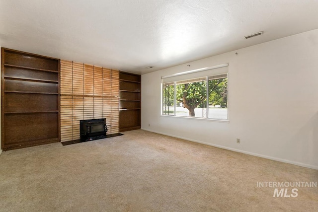 unfurnished living room with baseboards, carpet flooring, built in shelves, and a wood stove