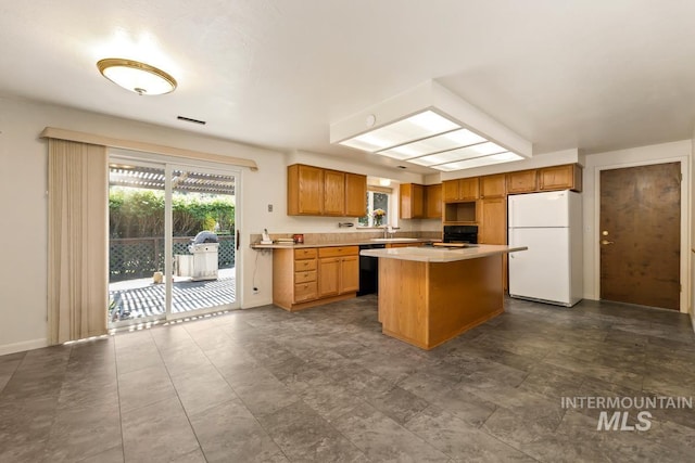 kitchen with freestanding refrigerator, a kitchen island, light countertops, dishwasher, and a sink