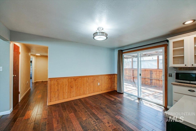 unfurnished dining area with dark wood finished floors, baseboards, a wainscoted wall, and wooden walls