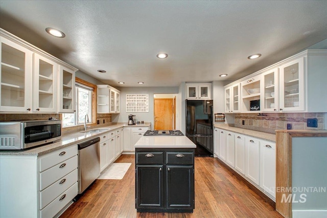 kitchen featuring white cabinets, a sink, dark cabinetry, a kitchen island, and appliances with stainless steel finishes
