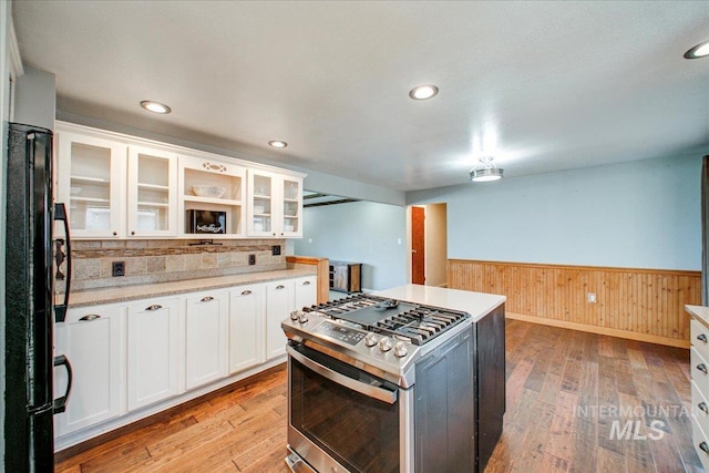 kitchen with white cabinets, a wainscoted wall, freestanding refrigerator, light wood-style floors, and gas stove